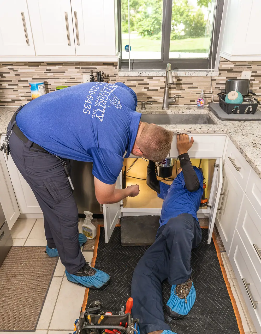 Integrity Plumbing technicians repairing a garbage disposal under a West Palm Beach kitchen sink